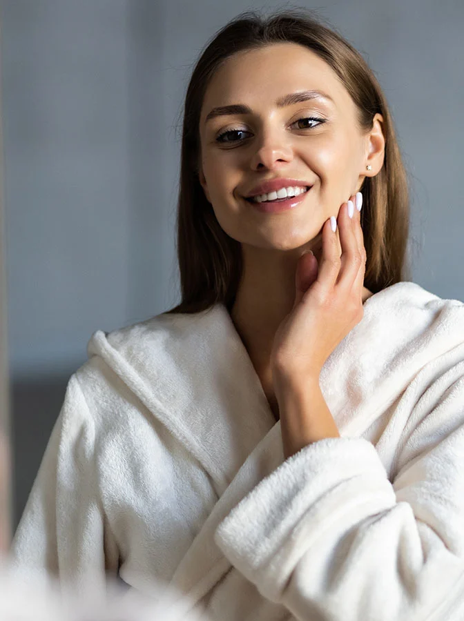 A young woman in a bathrobe smiles as she touches her face - Kybella for Double Chin in Balla Cynwyd, PA