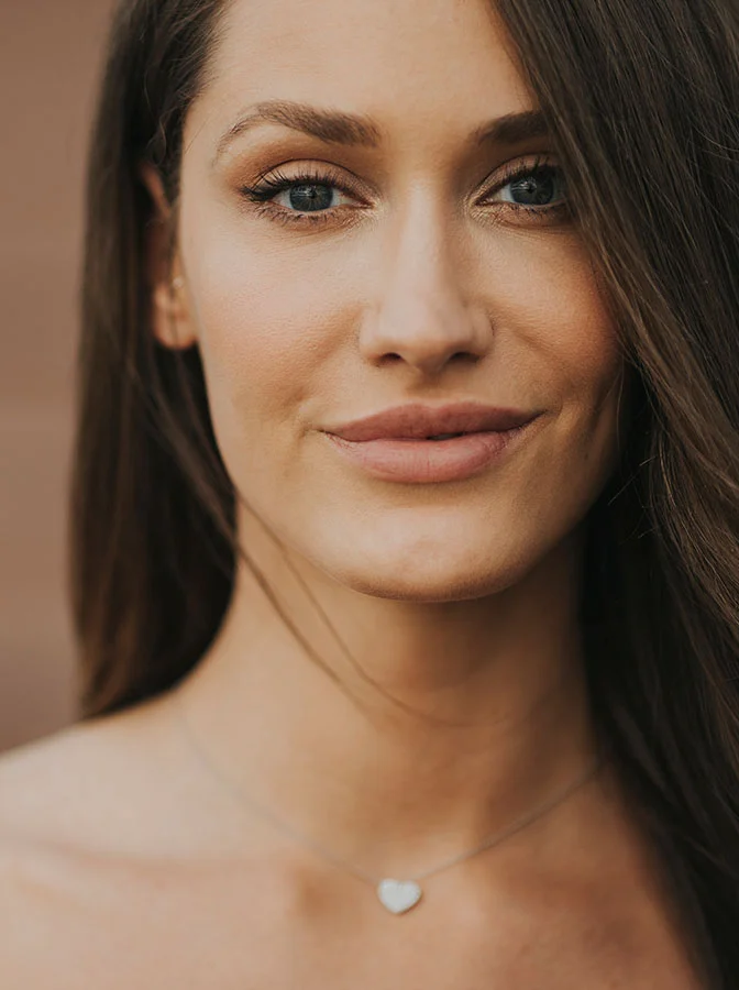 A close-up portrait of a smiling woman with light brown hair, wearing a small heart necklace - Lip Reduction in Bala Cynwyd, PA