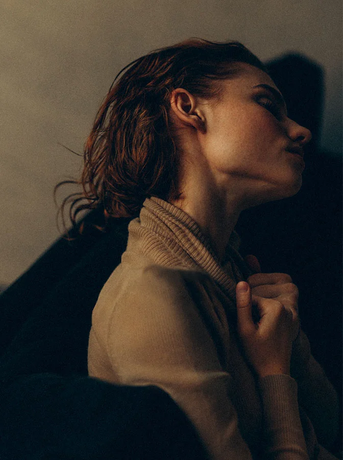 Close-up side profile of a woman with auburn hair, looking upwards with a soft light illuminating her face - Neck and Chin Liposuction in Bala Cynwyd, PA