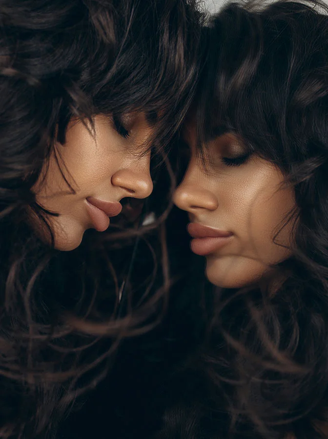 woman with voluminous wavy hair, their faces close together in a mirrored pose, highlighting their defined lips and facial features - Rhinoplasty in Bala Cynwyd, PA