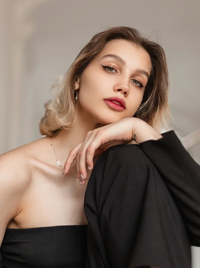 A young woman with styled blonde hair, wearing a strapless black dress, resting her head on her hand, with a poised, elegant expression - Tip Plasty in Bala Cynwyd, PA